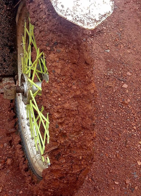 Red clay soil caked thickly onto a motorcycle wheel in the wet season